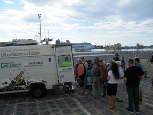 l'unità mobile dell' URP che stazione sulla banchina del porto di Porto Empedocle in  prossimità della nave e la fila dei crocieristi in attesa di ricevere informazioni.  